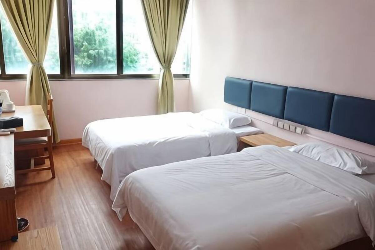 Quarto de hotel com duas camas, uma mesa e janela com cortinas.