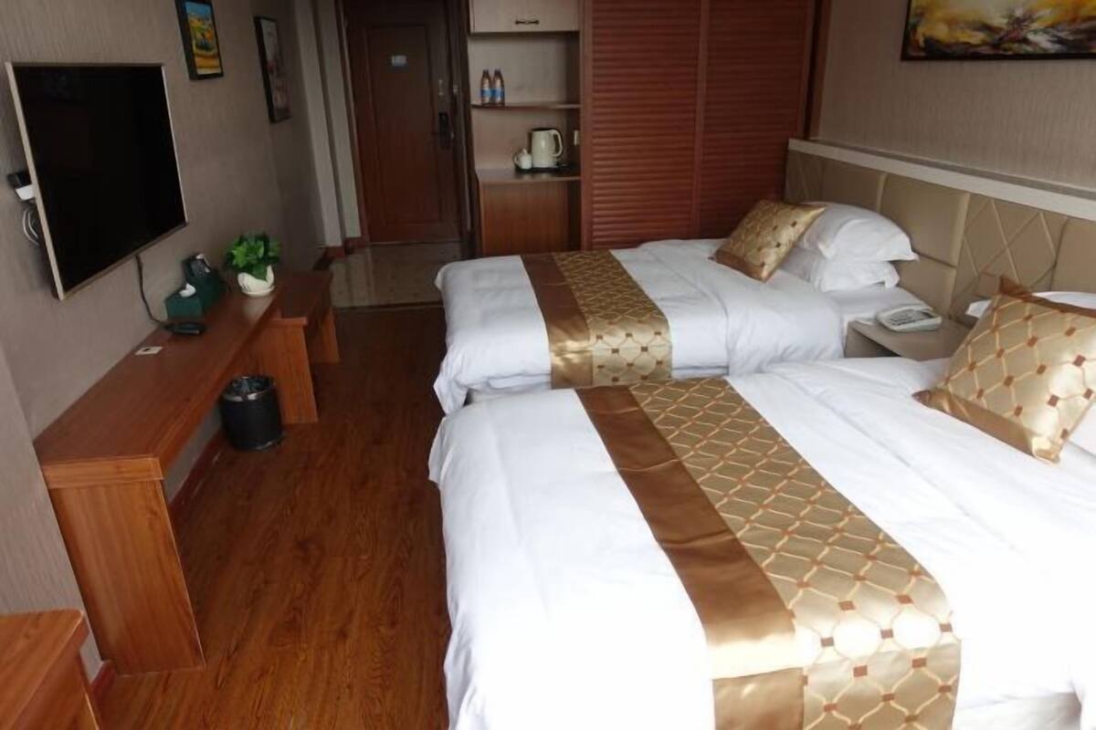 Quarto de hotel com duas camas, televisão, escrivaninha e guarda-roupa.
