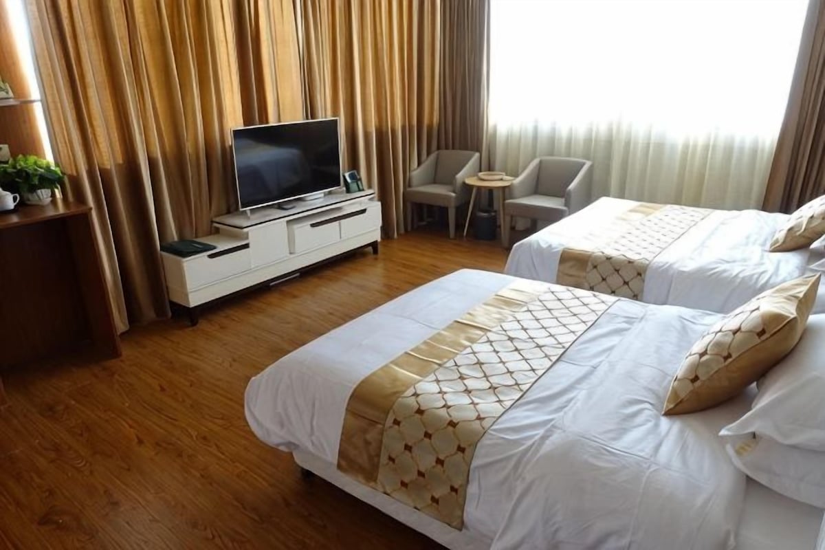 A hotel room with two beds, a TV on a dresser, a small table, and a chair.
