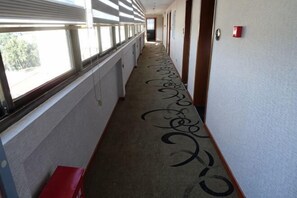 A hotel corridor with a carpeted floor, a red bench, and a fire alarm on the wall.