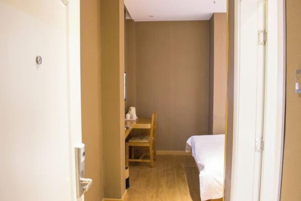 Ein schmaler Flur, der zu einem Zimmer mit einem Bett, einem Sessel und einem kleinen Tisch mit Wasserkocher führt.