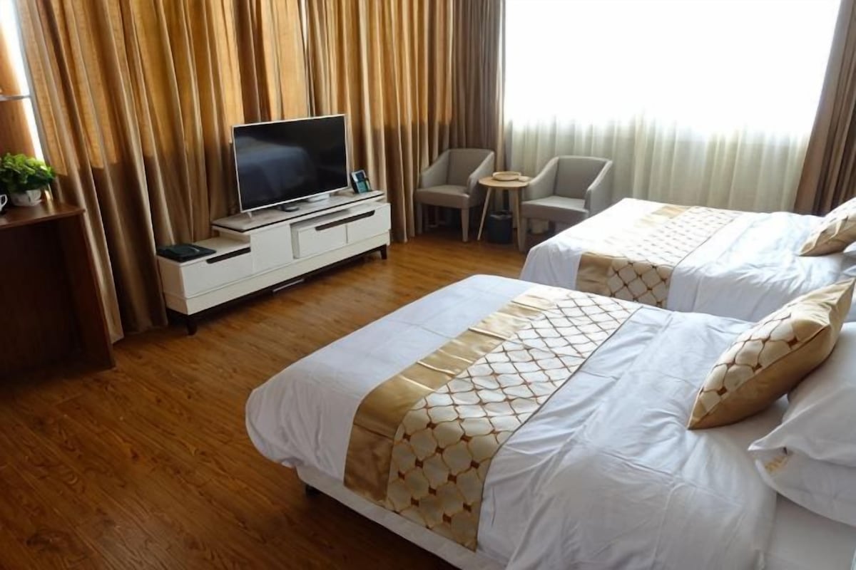 A hotel room with two beds, a television on a dresser, a small table, and a chair.