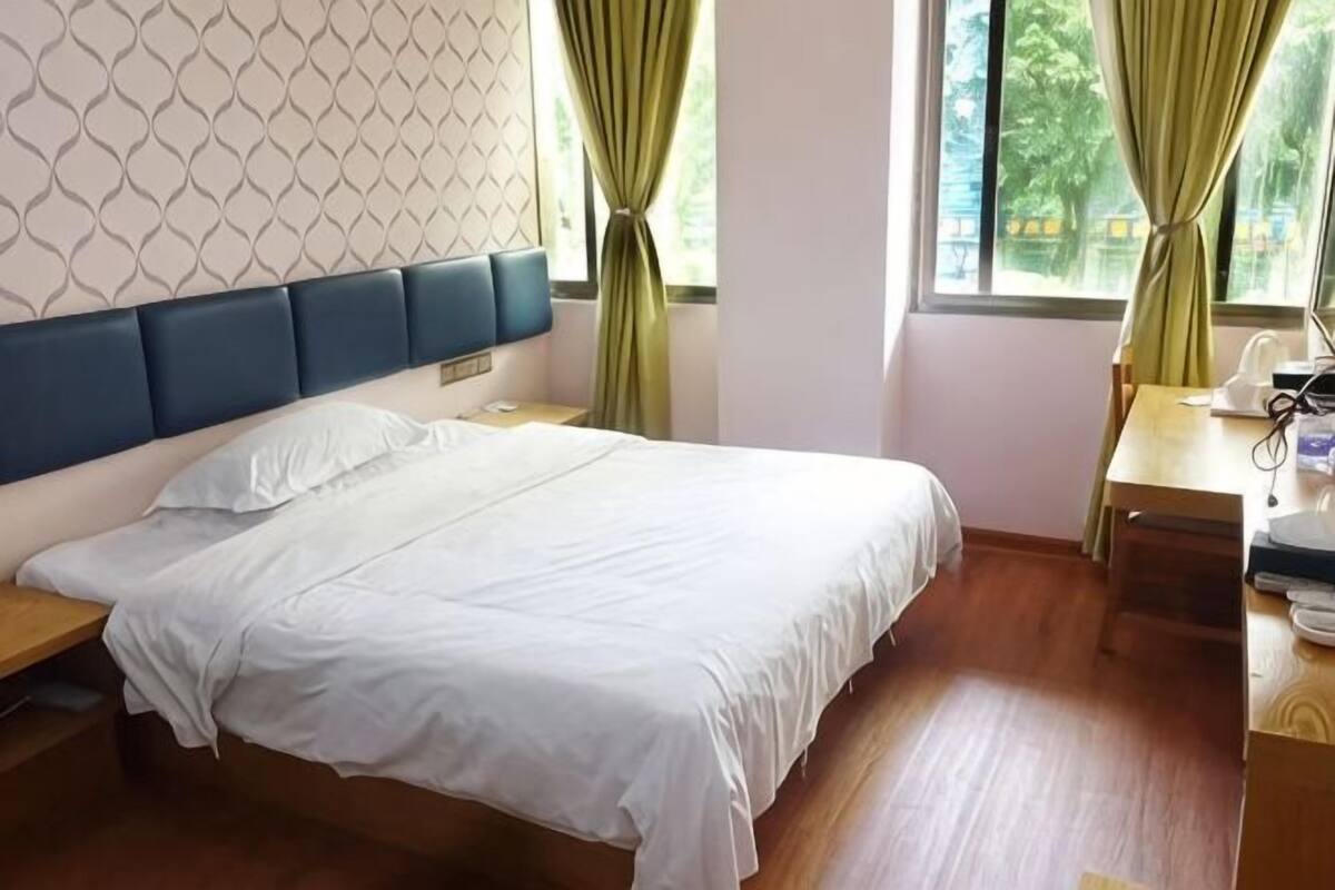 Um quarto com uma cama, mesas de cabeceira, uma escrivaninha e uma janela com cortinas.