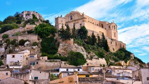 A historic building on a hill with traditional architecture, surrounded by a small town with terracotta-roofed houses. - Villa Milizie (Scicli)