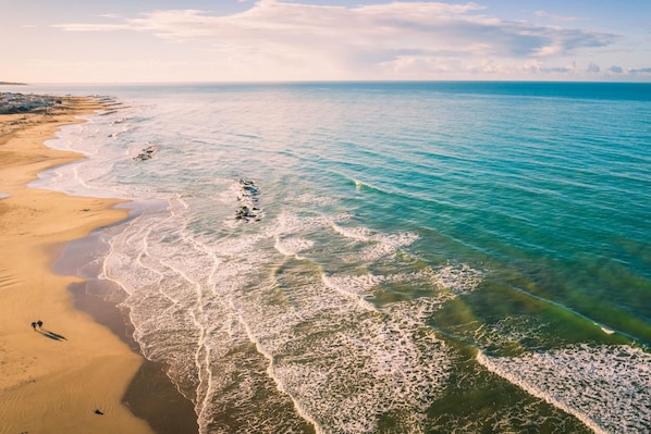 An aerial view of a beach with clear turquoise waters and a sandy shoreline.