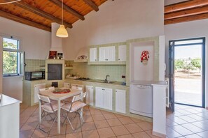 Una cocina con armarios blancos, una mesa de comedor con sillas, un microondas, un fregadero y un refrigerador.