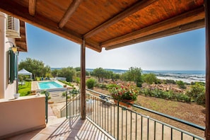 Un balcón con vistas a una piscina, jardín y paisaje distante.