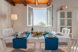 Mesa de comedor servida con platos, vasos y una botella, con una ventana y un armario al fondo.