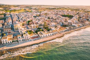 An aerial view of a coastal town with a dense cluster of buildings along the waterfront, a promenade, and a clear view of the sea.