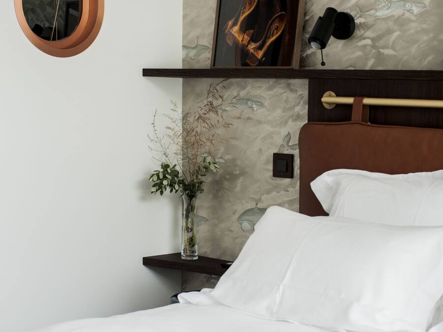 Una camera da letto con un letto, un comodino con un vaso di piante essiccate, uno scaffale a parete con un quadro e una lampada a parete.