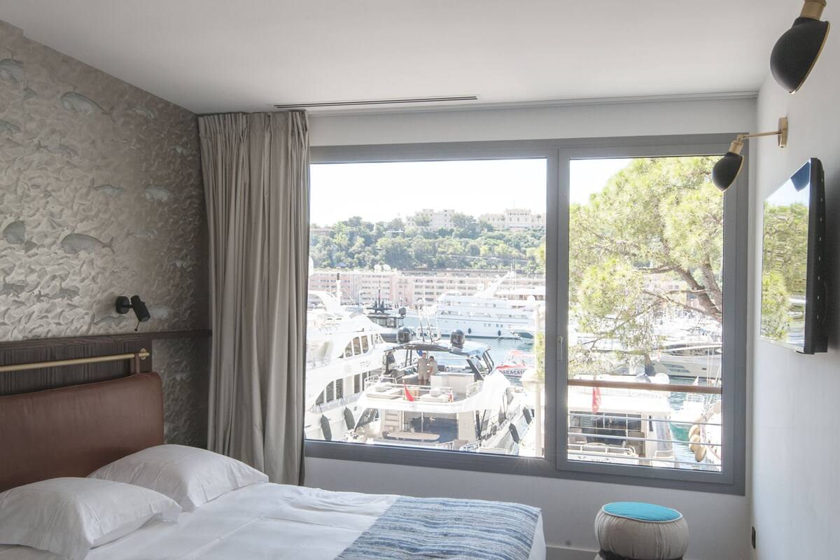 A bedroom with a large window, a bed, a stone wall, and a wooden floor.