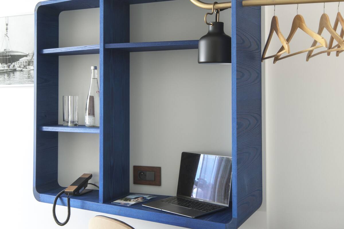 A room with a blue built-in desk, a chair, a laptop, a hanging lamp, and a coat rack.