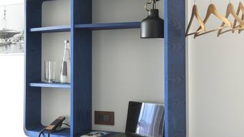Una habitación con un escritorio azul empotrado, una silla, una computadora portátil, una lámpara colgante y un perchero.