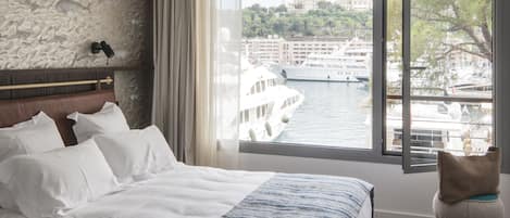A bedroom with a large bed, a stone wall, a view of a body of water, and a window with curtains.