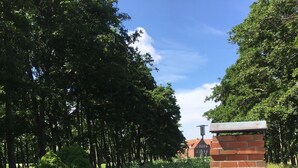 A brick outdoor oven with a chimney, surrounded by lush greenery and a well-maintained lawn.