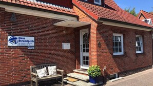 A red brick building with a sign for 'Haus Strandperle' and a bench outside.