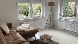A living room with a brown sofa, a glass coffee table, and two windows with blinds.