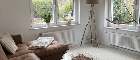 Ein Wohnzimmer mit einem braunen Sofa, einem Glastisch und zwei Fenstern mit Jalousien.