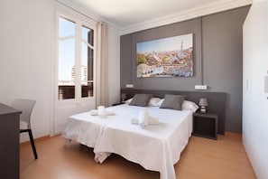 Quarto de hotel com cama, duas mesas de cabeceira, escrivaninha e uma janela grande.
