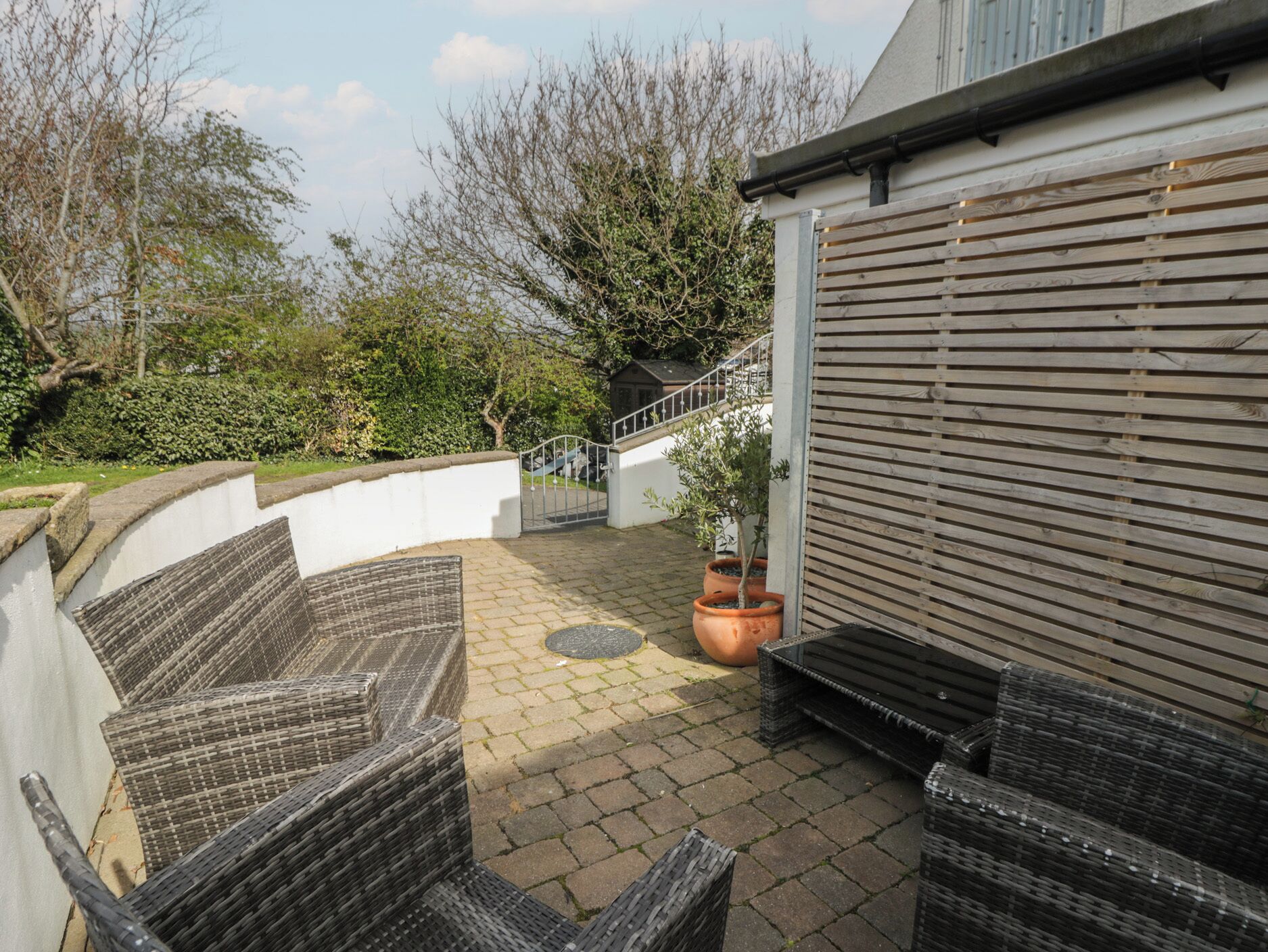 An outdoor patio with wicker furniture, a potted plant, and a white wall.