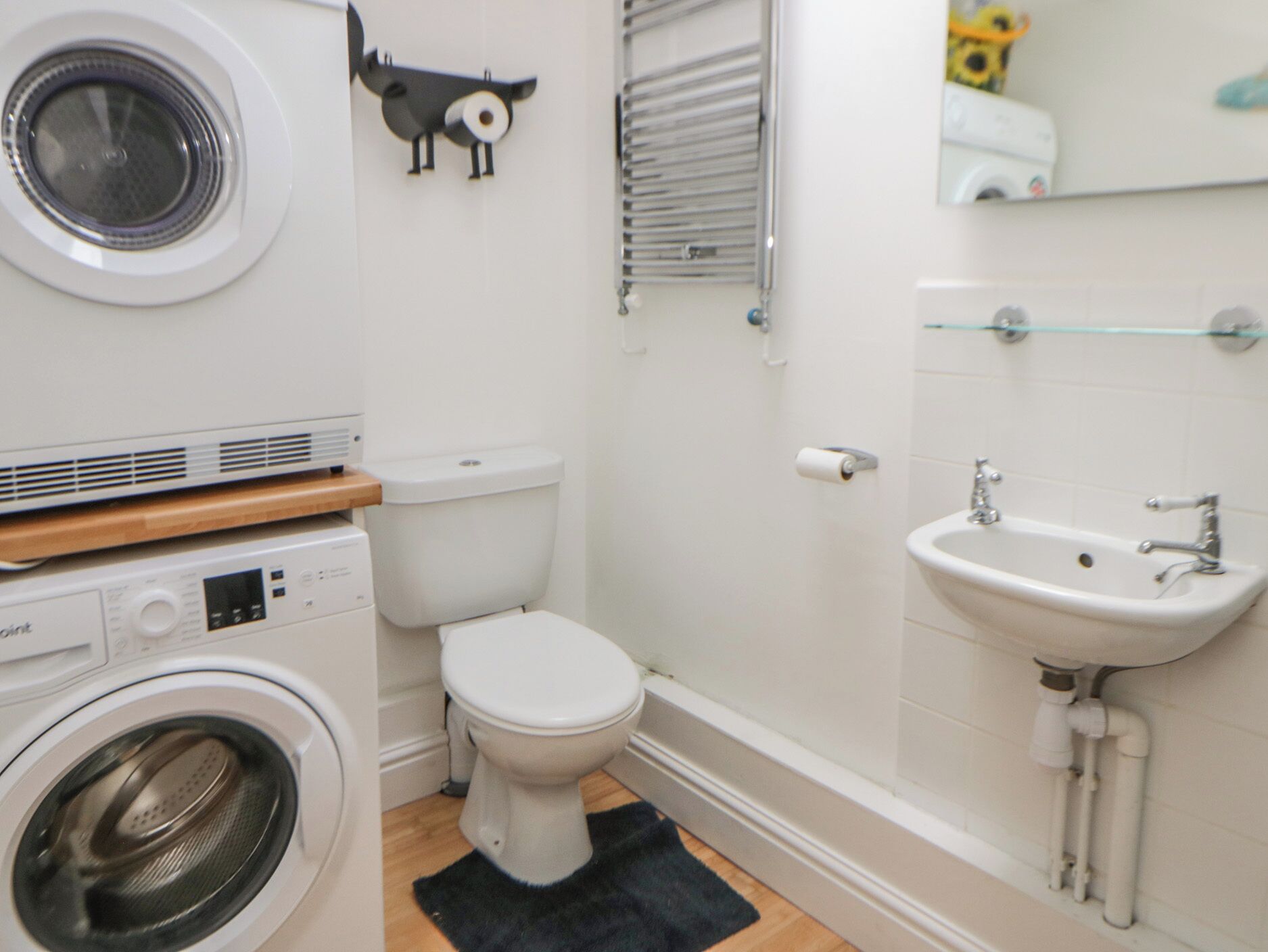 A compact bathroom with a washing machine, toilet, sink, and a small mirror.