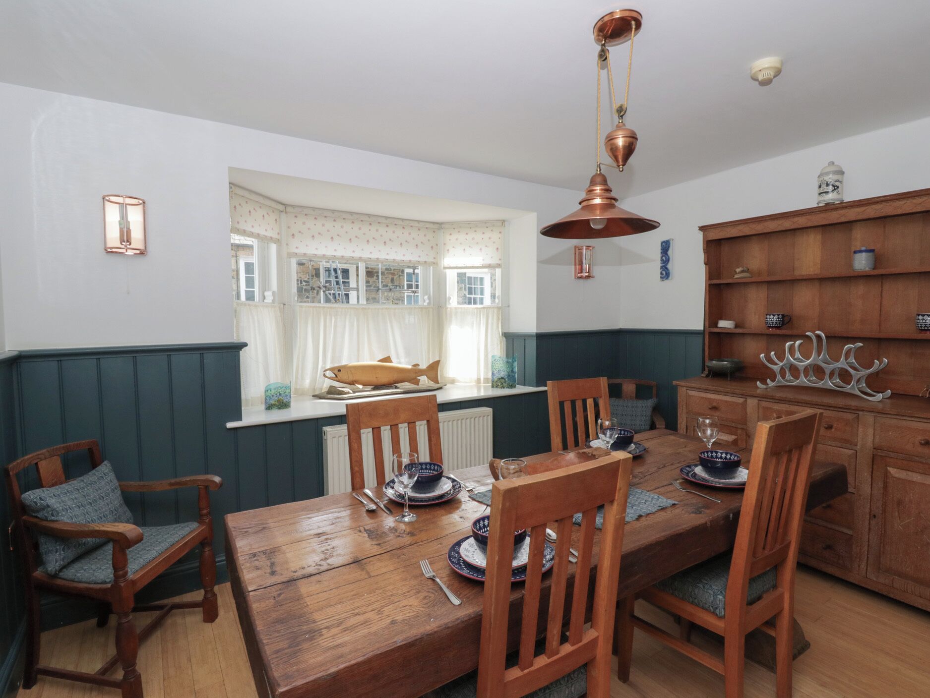 Uma área de refeições com uma mesa de madeira, cadeiras e um modelo de peixe no parapeito da janela.