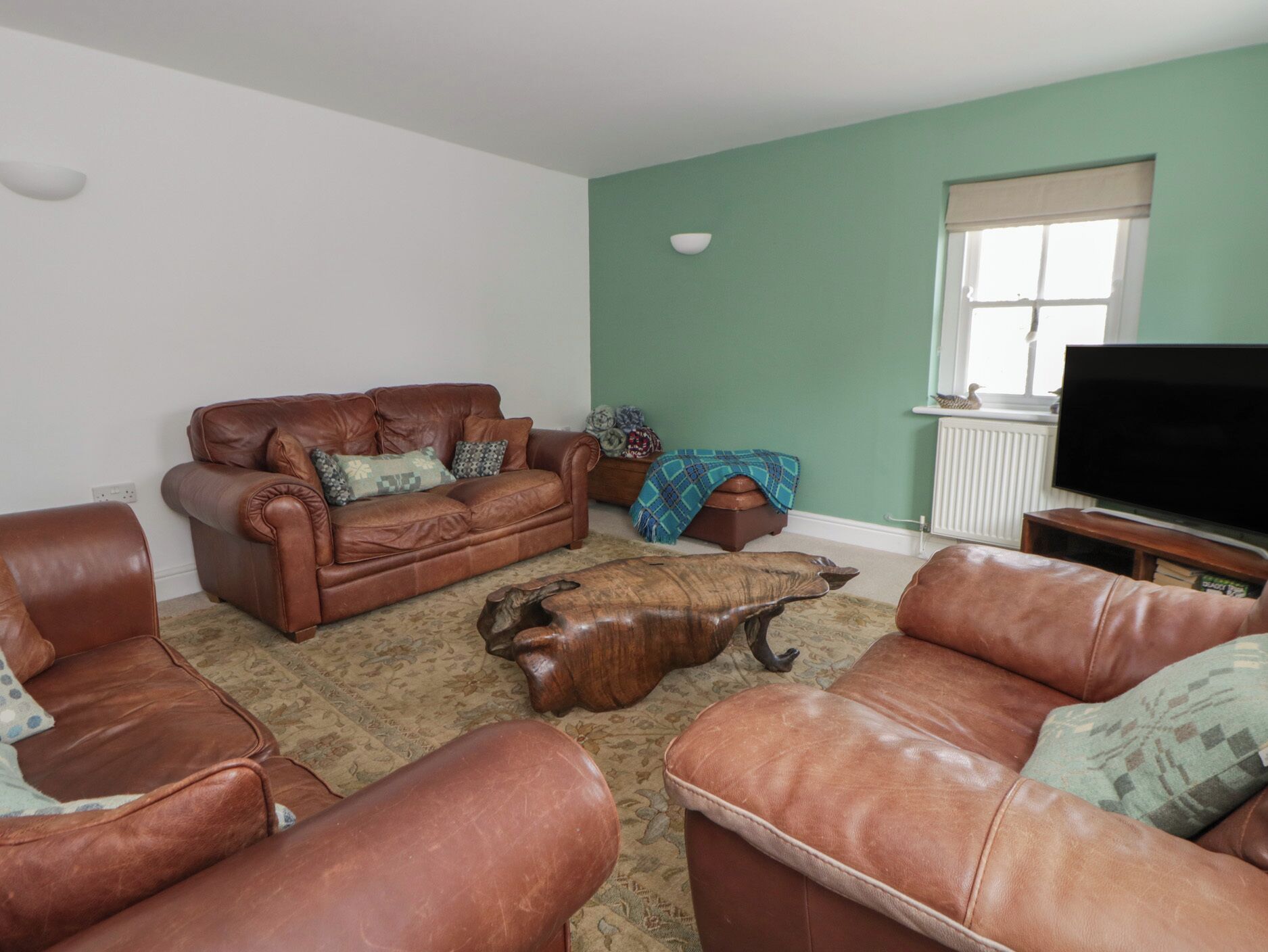 A living room with a brown leather sofa, a wooden coffee table, and a television on a stand.