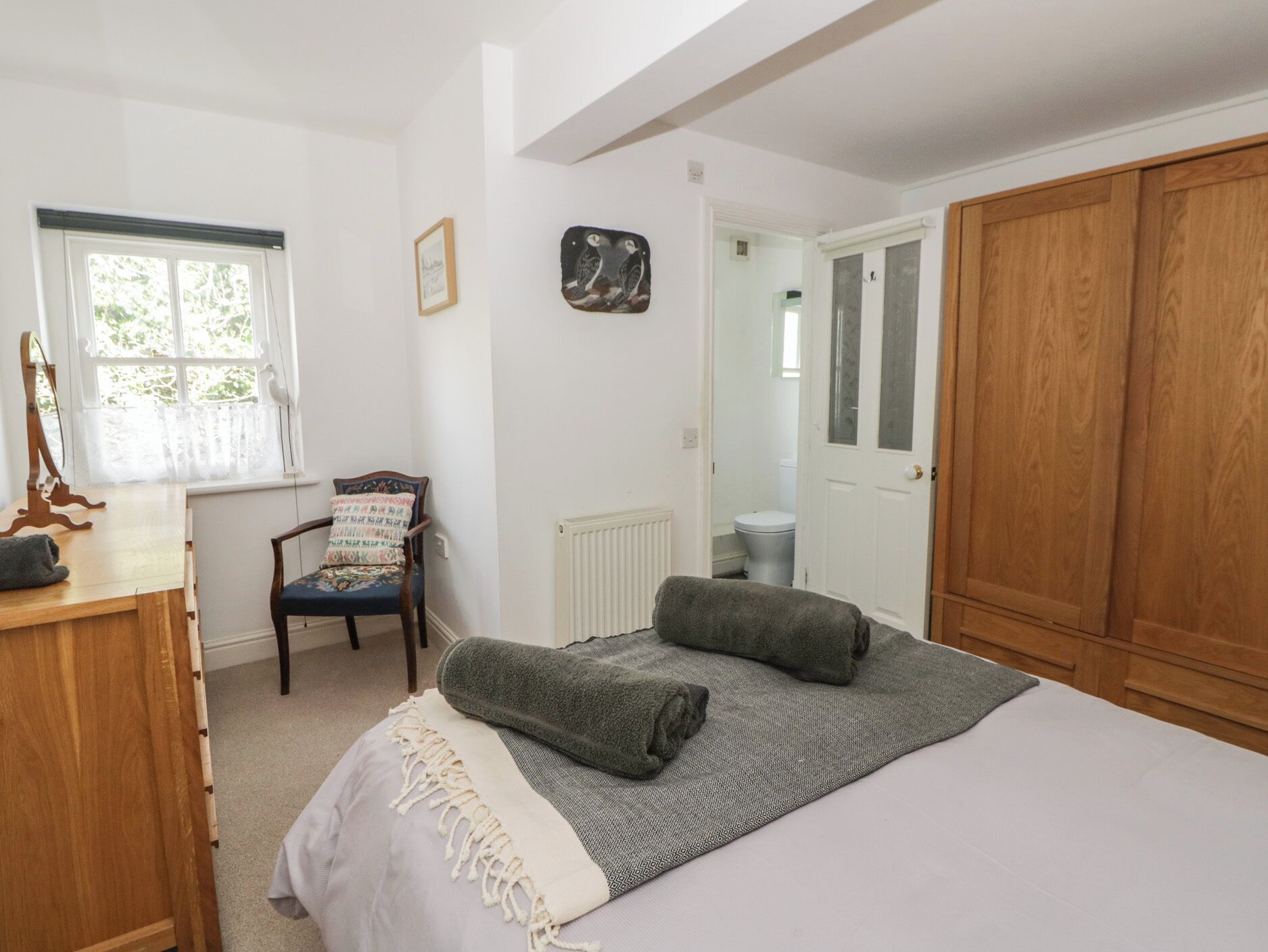 A bedroom with a bed, a wooden wardrobe, a chair, a radiator, and a window.