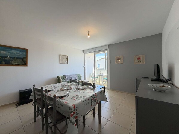 Un coin repas avec une table dressée pour quatre personnes, un canapé, un téléviseur posé sur un meuble et un tableau accroché au mur.