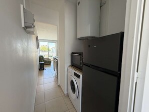 A compact kitchen with a washing machine, a microwave, and a refrigerator.