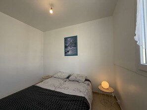 Une chambre à coucher avec un lit, une table de chevet avec une lampe, un tableau au mur et une fenêtre avec des rideaux.