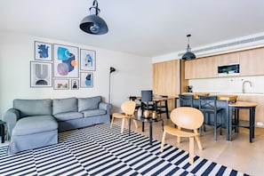 Un salon moderne avec un canapé gris, un tapis rayé noir et blanc et un coin repas comprenant des chaises en bois et une table noire.