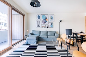 Un salon moderne avec un canapé d’angle, un tapis à carreaux noirs et blancs et une vue sur la ville à travers de grandes fenêtres.