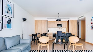 A modern living room with a sofa, a dining area with chairs and a table, and a kitchen with wooden cabinets and appliances. - Gelman's Getaway in Lisbon (Lisbon)