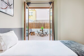 A hotel room with a bed, a small balcony with a table and chairs, and a view of the outside buildings. - Gelman's Getaway in Lisbon (Lisbon)