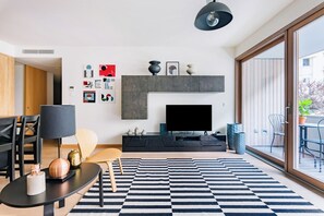 A modern living room with a flat-screen TV, a black and white striped rug, and a dining area with a table and chairs. - Gelman's Getaway in Lisbon (Lisbon)