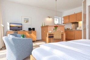 Et moderne hotelværelse med seng, skrivebord, stol, fjernsyn og et tekøkken.