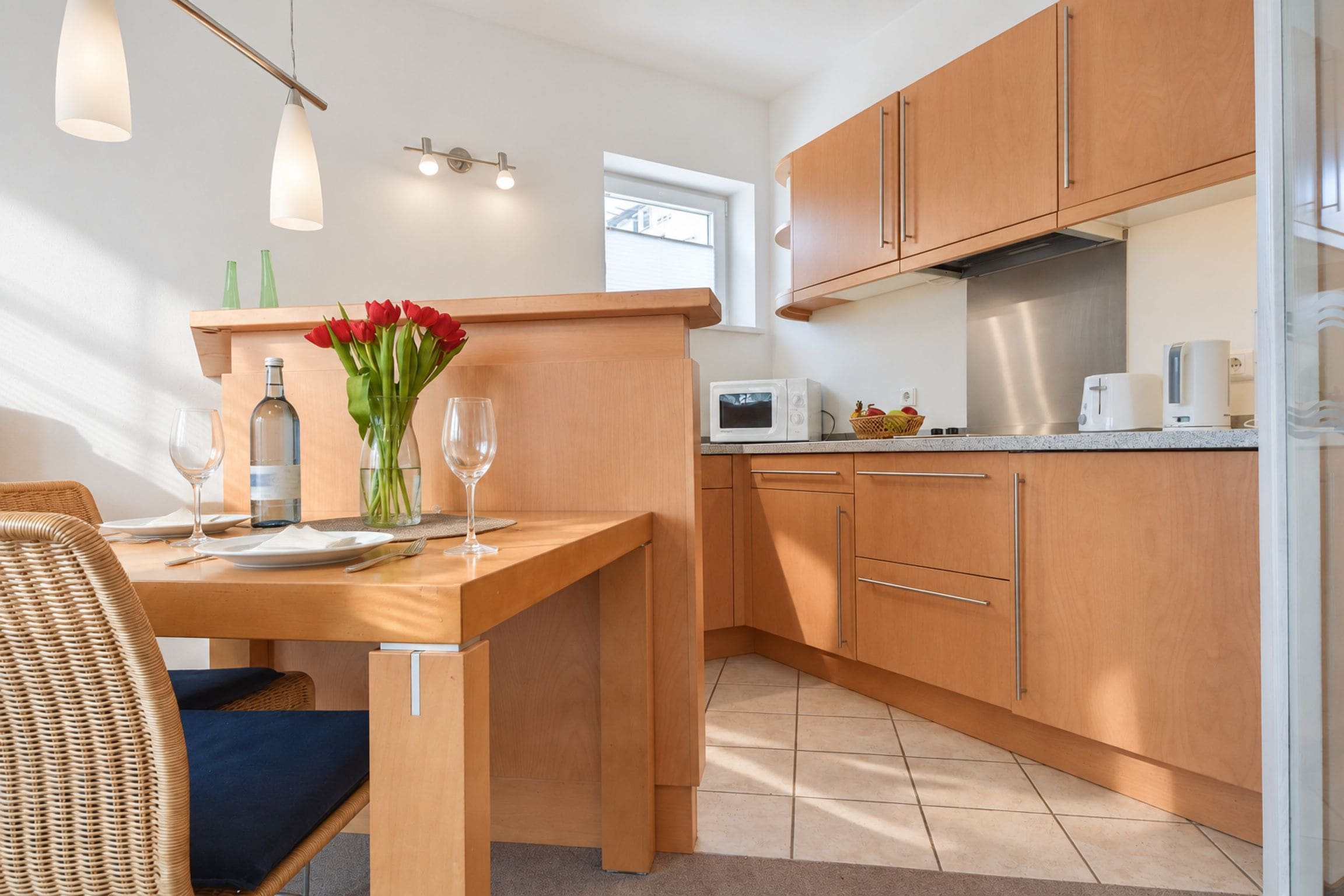 A modern kitchen with wooden cabinets, a dining table with chairs, and a window providing natural light.