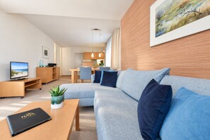 A modern living room with a sectional sofa, a coffee table, a TV, and a dining area in the background. - House Ardenne 01 - only a few meters to the fine sandy Baltic Sea beach (Heringsdorf (Seebad))