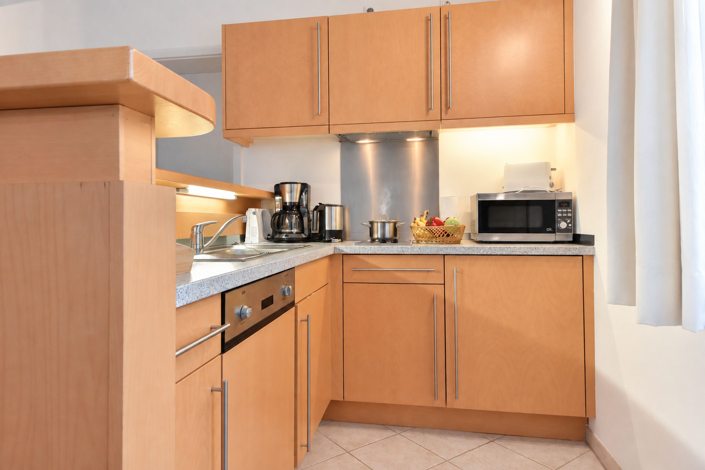 Een kleine keuken met houten kastjes, een koffiezetapparaat, een magnetron en een spoelbak.
