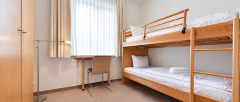 Une chambre avec un lit superposé, un bureau et une chaise, une fenêtre avec des rideaux et une armoire.