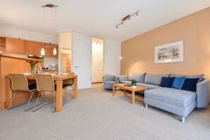 Una sala de estar moderna con un sofá gris, un comedor con muebles de madera y una cocina con armarios de madera.