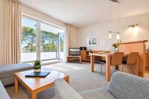 Une chambre d’hôtel moderne équipée d’un canapé, d’une table à manger avec des chaises, d’une télévision et d’un balcon avec des rideaux.