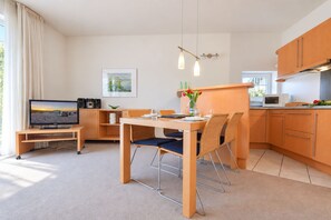 Una cocina moderna con armarios de madera, una mesa de comedor con sillas, un televisor y un cuadro en la pared.