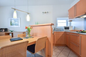 A modern kitchen with wooden cabinets, a dining table with wicker chairs, a small island, and a microwave. - House Ardenne 04 - only a few meters to the fine sandy Baltic Sea beach (Heringsdorf (Seebad))