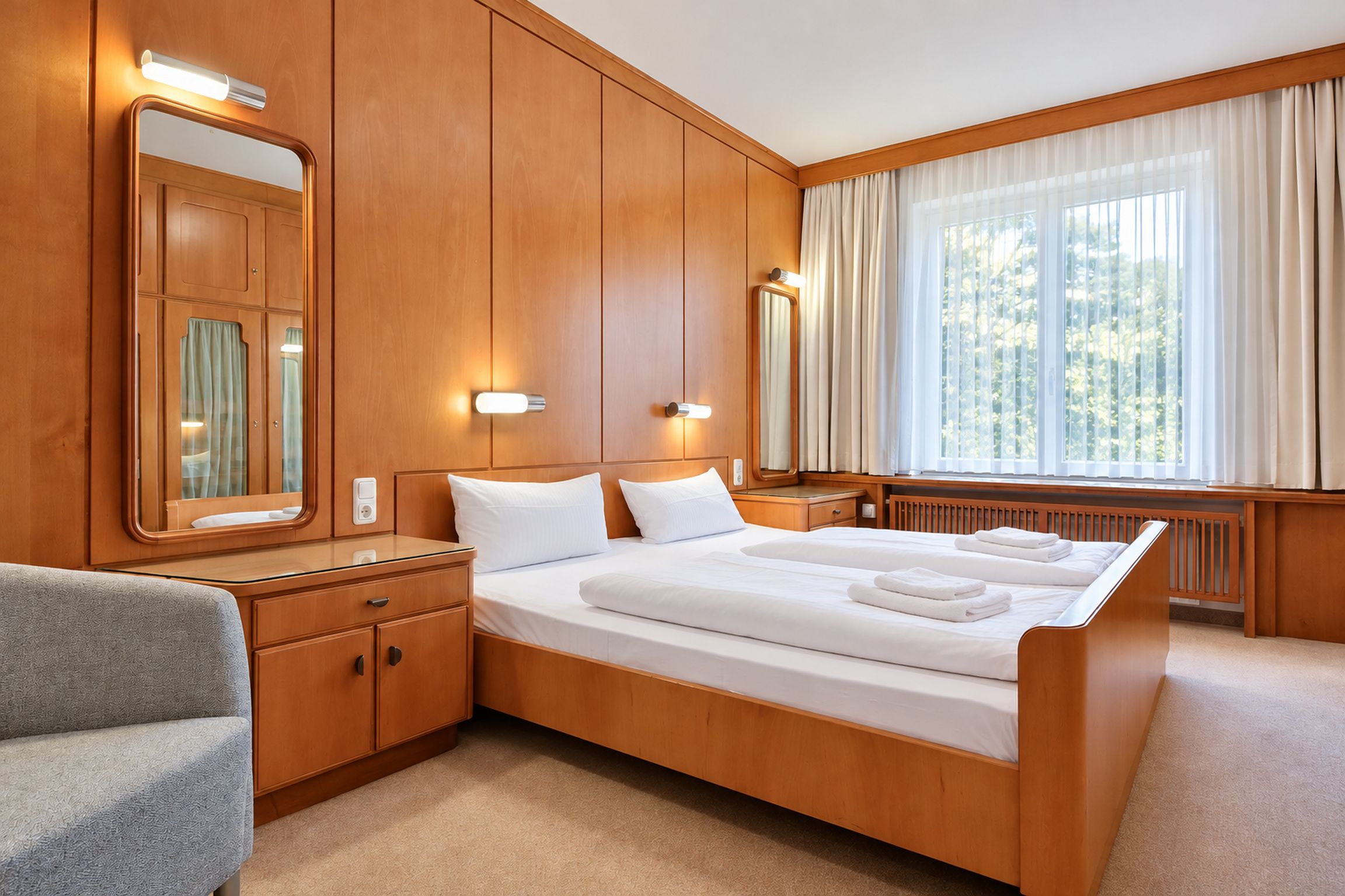 A hotel room with a large bed, wooden paneling, a sitting area with a chair, and a window with curtains.