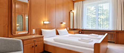 Habitación de hotel con una cama grande, paneles de madera, un rincón de descanso con una silla y una ventana con cortinas.