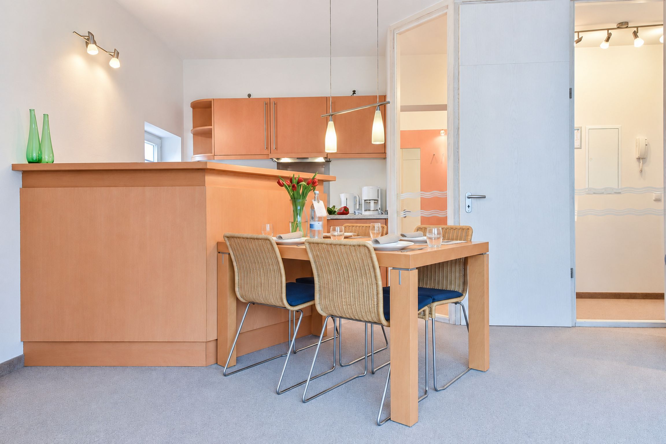 Een compacte keuken met een centraal eiland, twee stoelen en een eettafel.
