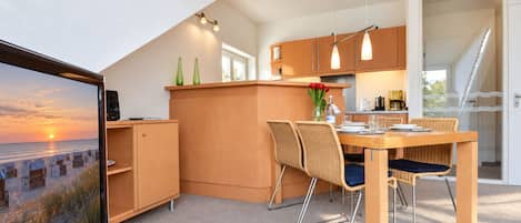 Une cuisine moderne avec des meubles en bois, un coin repas avec des chaises en osier et une grande fenêtre donnant sur une plage.