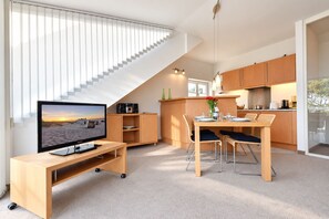 A modern kitchen with a dining area, a TV on a stand, and a staircase leading to an upper level. - House Ardenne 07 - perfect beach location with balcony and Baltic Sea view (Heringsdorf (Seebad))